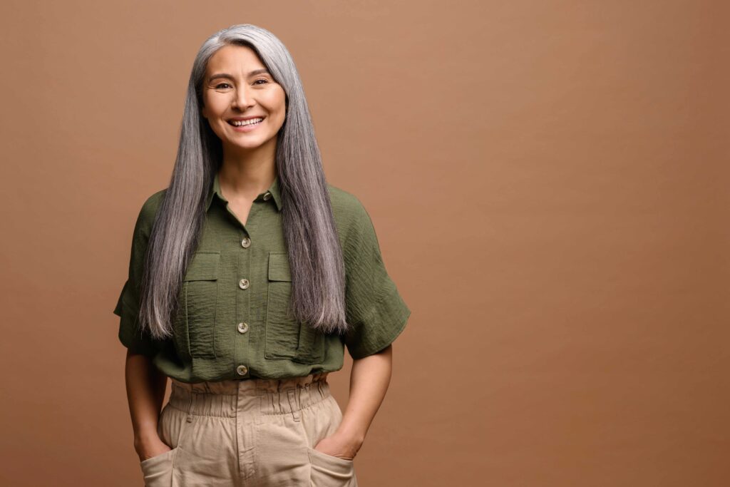 A confident, smiling woman with long gray hair symbolizes the balanced well-being achieved through hormone therapy at Premiere Concierge & Wellness.