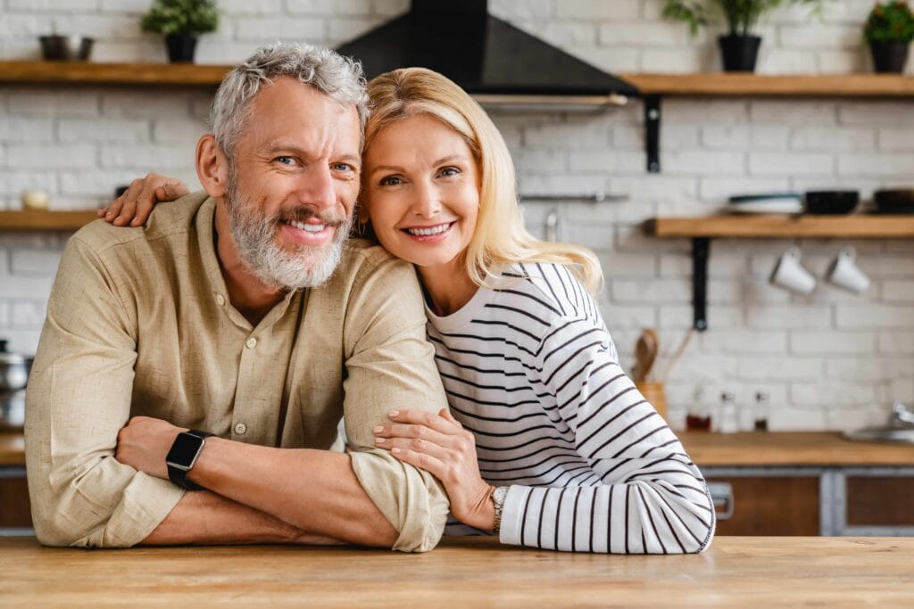 A happy, healthy couple in a cozy kitchen setting, representing the balance and vitality achieved through hormone therapy at Premiere Concierge & Wellness.