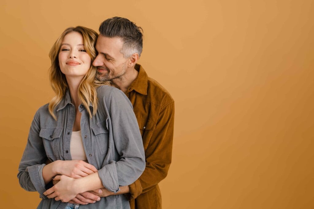 A happy couple embracing against a warm background, symbolizing vitality and balance, showcasing how hormone replacement therapy can help with weight loss and overall well-being