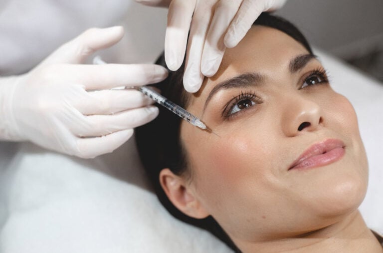 A woman with smooth skin lies on a treatment bed while a professional wearing gloves carefully administers botox under your eyes with a fine needle, targeting fine lines and wrinkles for a refreshed and youthful appearance.