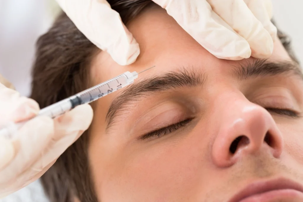 A man receiving a cosmetic injection in his forehead during a non-surgical procedure, illustrating how about a BOTOX® brow lift can enhance the appearance of the eye area by lifting drooping brows.