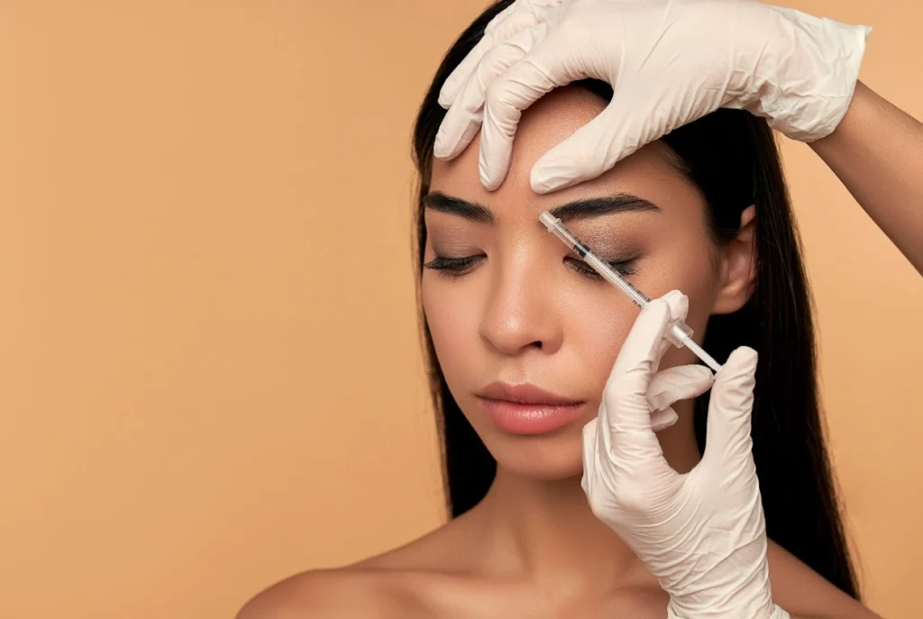 A woman receives a forehead injection from a medical professional wearing gloves, illustrating a common treatment area discussed in the comparison of dysport® vs botox® for wrinkle reduction.