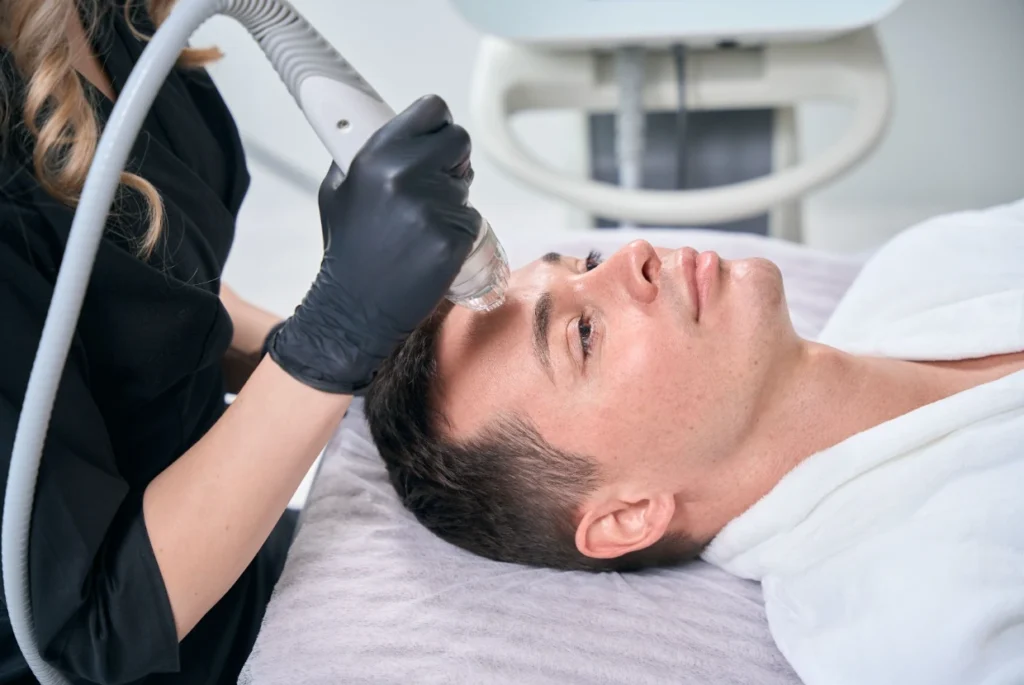 A man receives a facial treatment with a radiofrequency microneedling device administered by a professional, showcasing one of the key RF microneedling benefits—skin rejuvenation with minimal downtime.